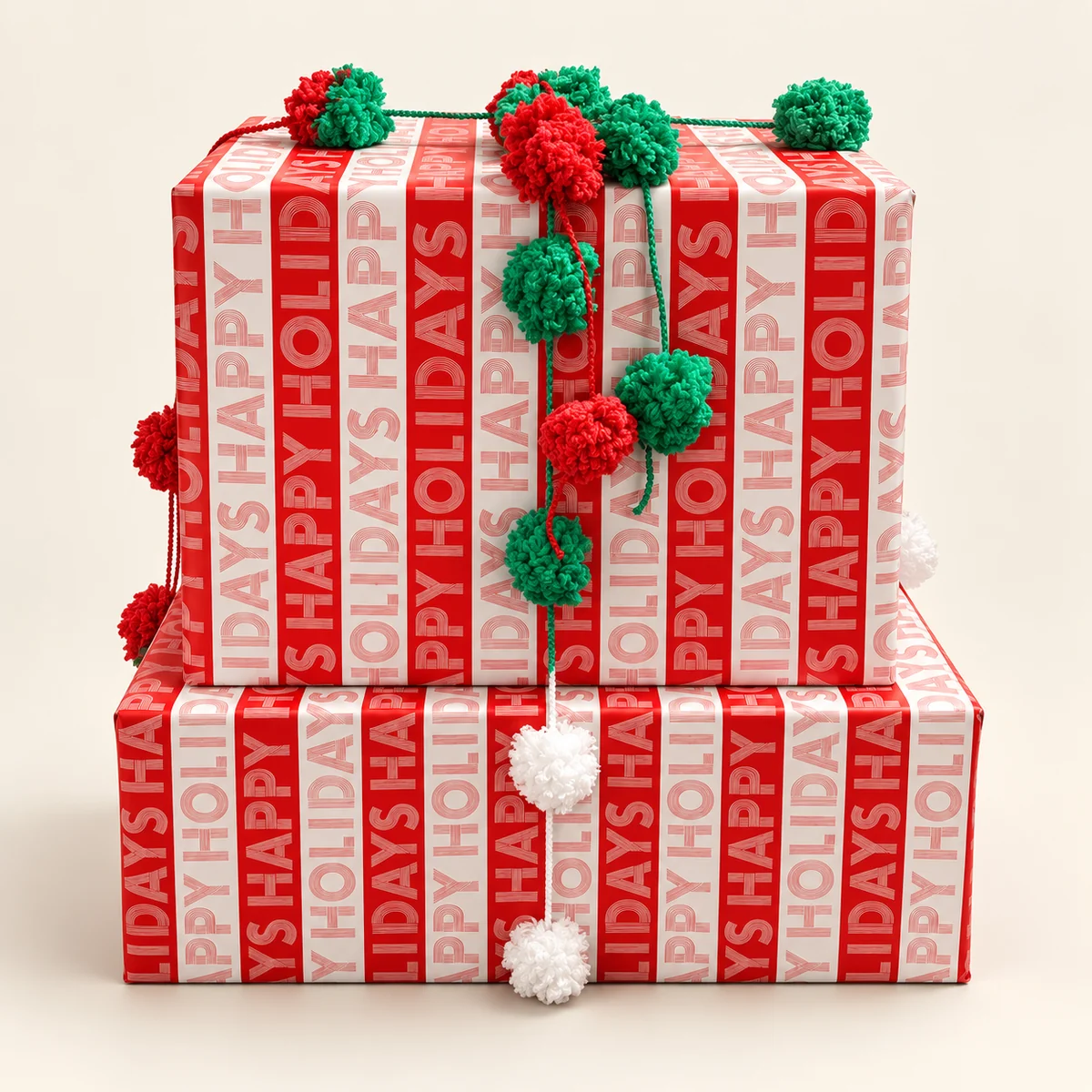 Two stacked boxes in red Happy Holidays paper with a pom-pom garland